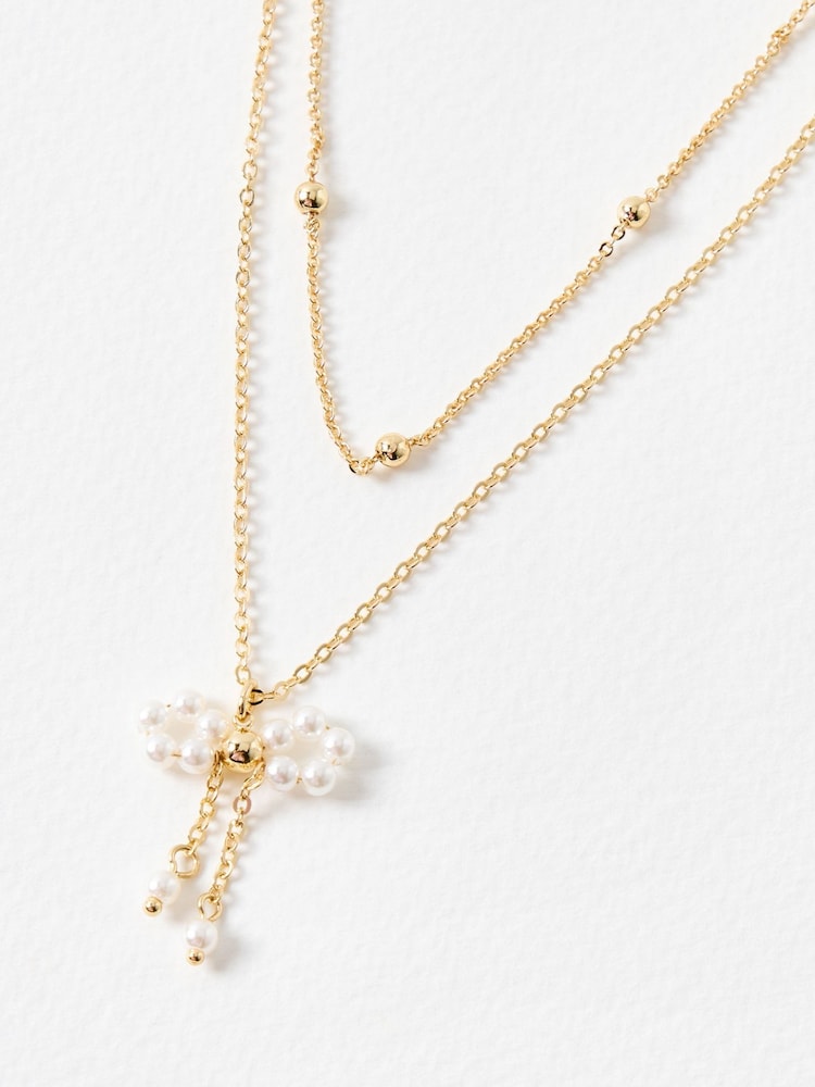 Oliver Bonas Gold Tone Aelia Faux Pearl Bow Layered Necklace - Image 1 of 4 Oliver Bonas Gold Tone Aelia Faux Pearl Bow Layered Necklace - Image 1 of 4