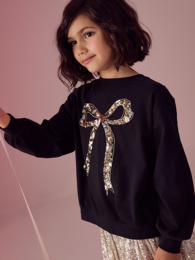 Black/Gold Sequin Bow Long Sleeve Wrap Back 100% Cotton Top (3-16yrs) - Image 1 of 4